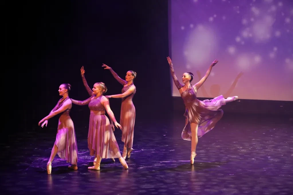 Ballet dancers performing on stage under purple lights