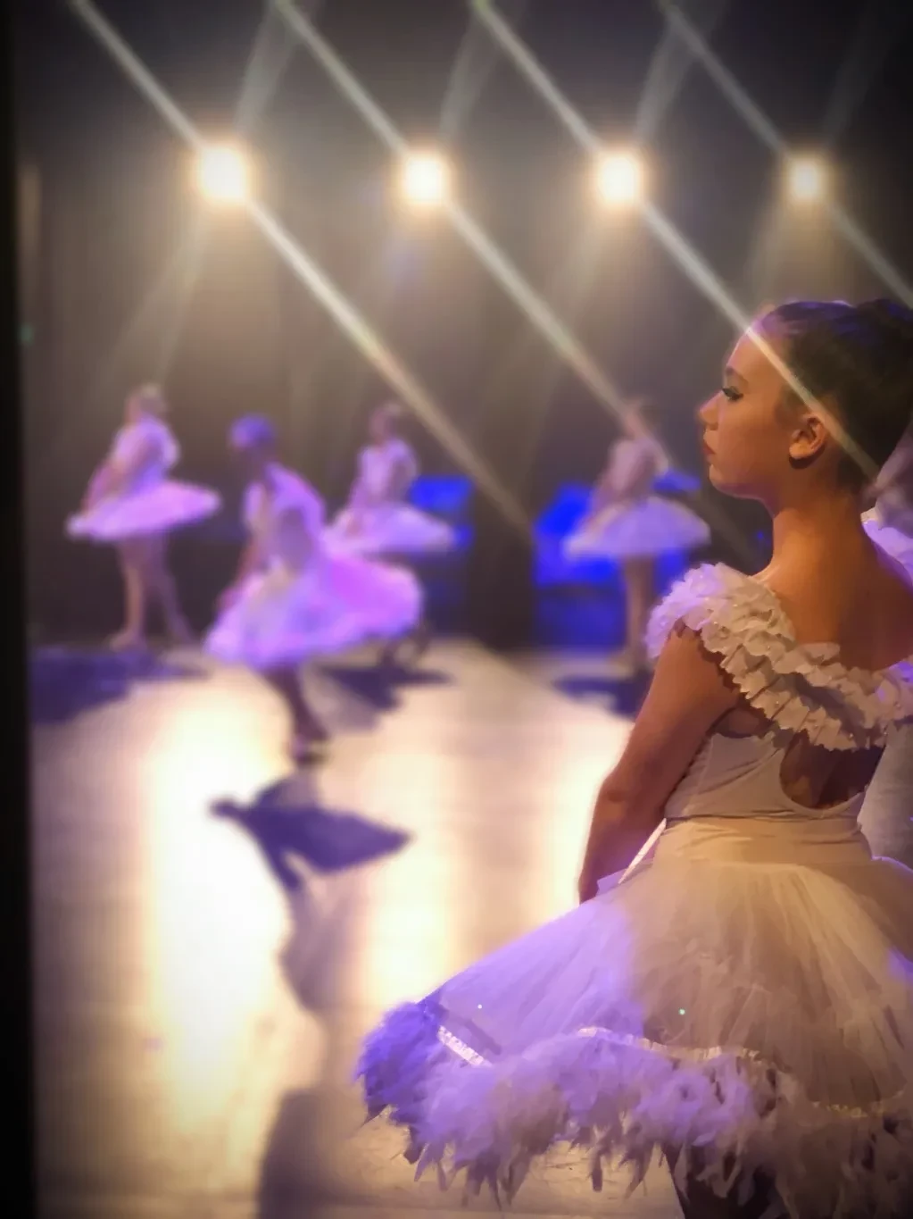 Young ballet dancer in white feathered tutu watching from the wings
