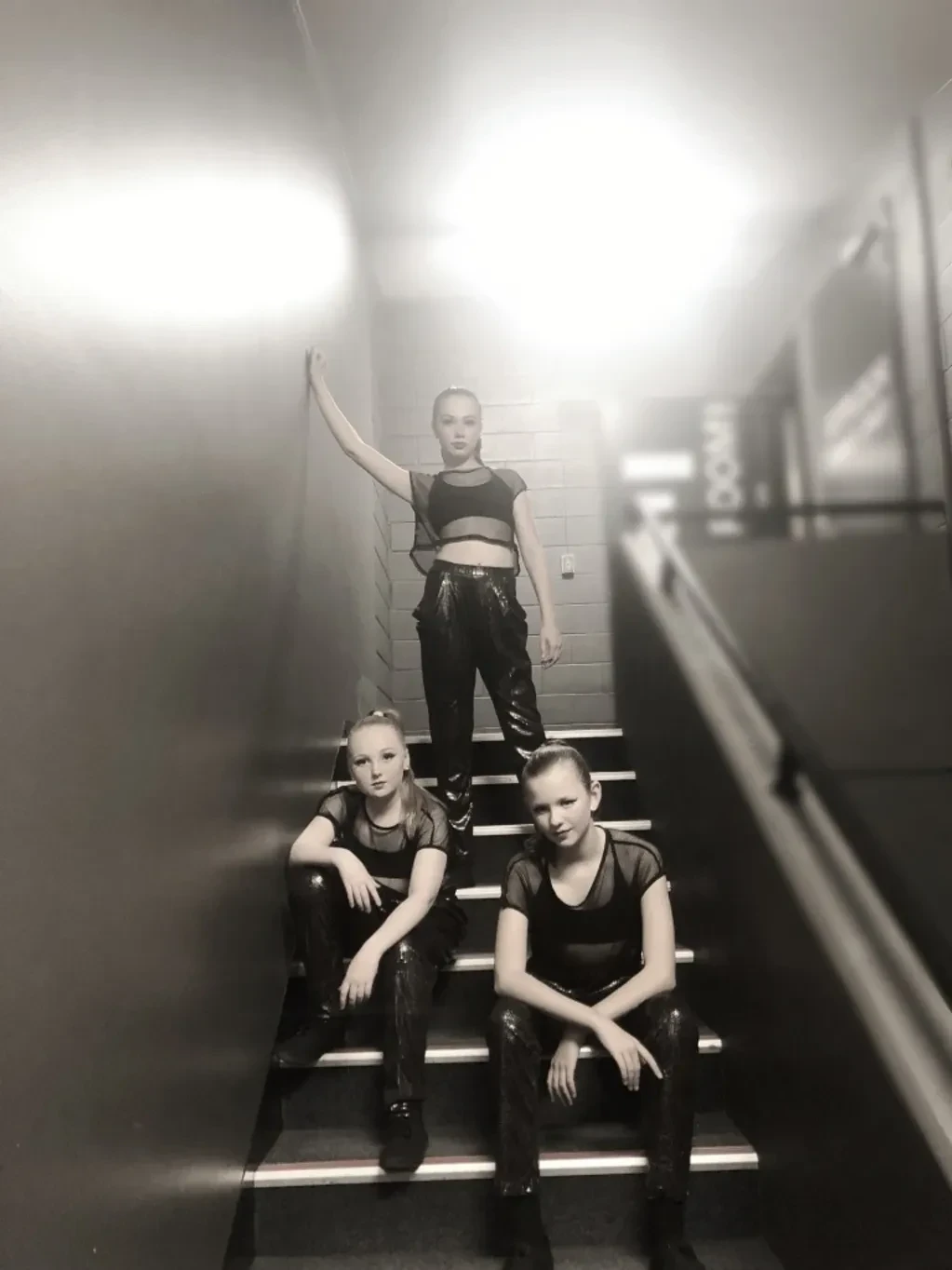 Three dancers in black outfits posed on staircase in black and white