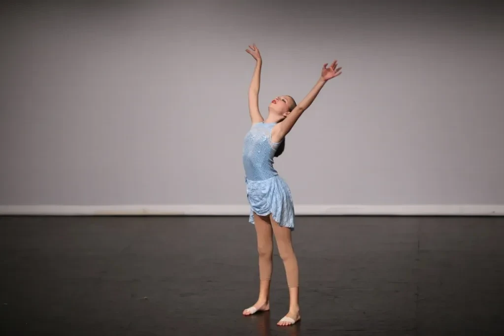 Young dancer in blue costume reaching upward on stage