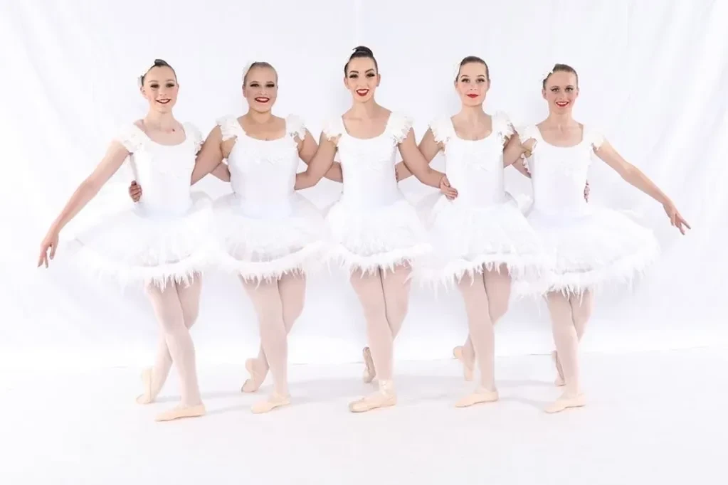 Five ballet dancers in white feathered tutus standing in a line