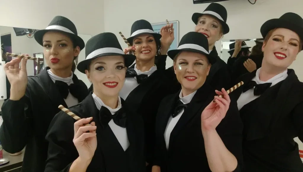 Group of women in black tuxedo jackets and top hats backstage