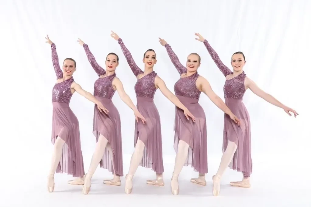 Five dancers in purple sequin and chiffon costumes posed in a line