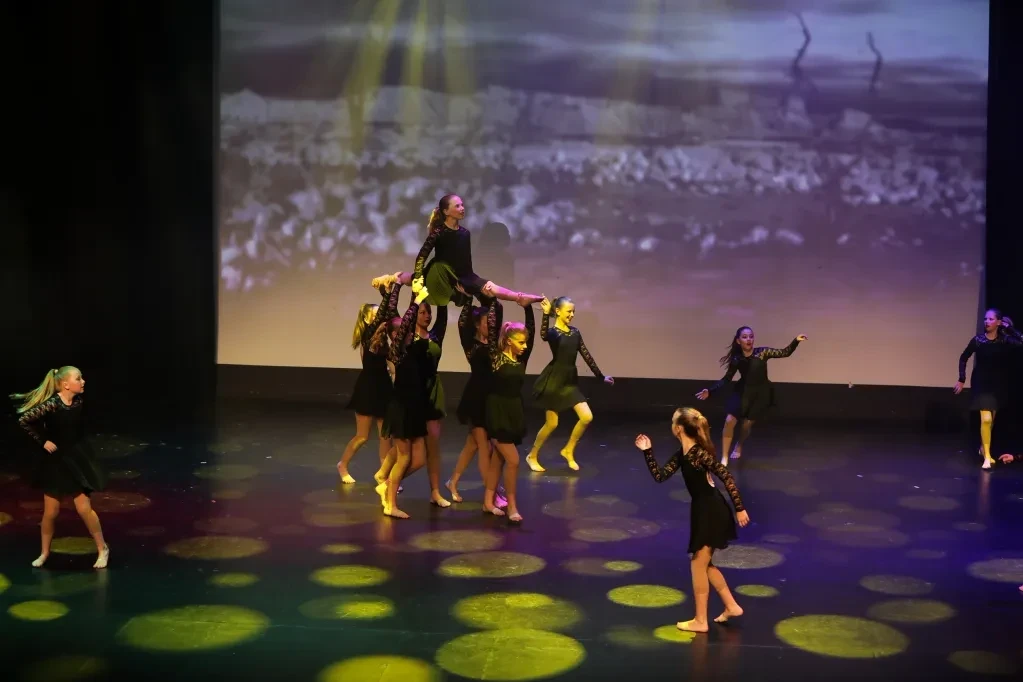 Contemporary dance group in black lifting a dancer overhead with projected landscape backdrop