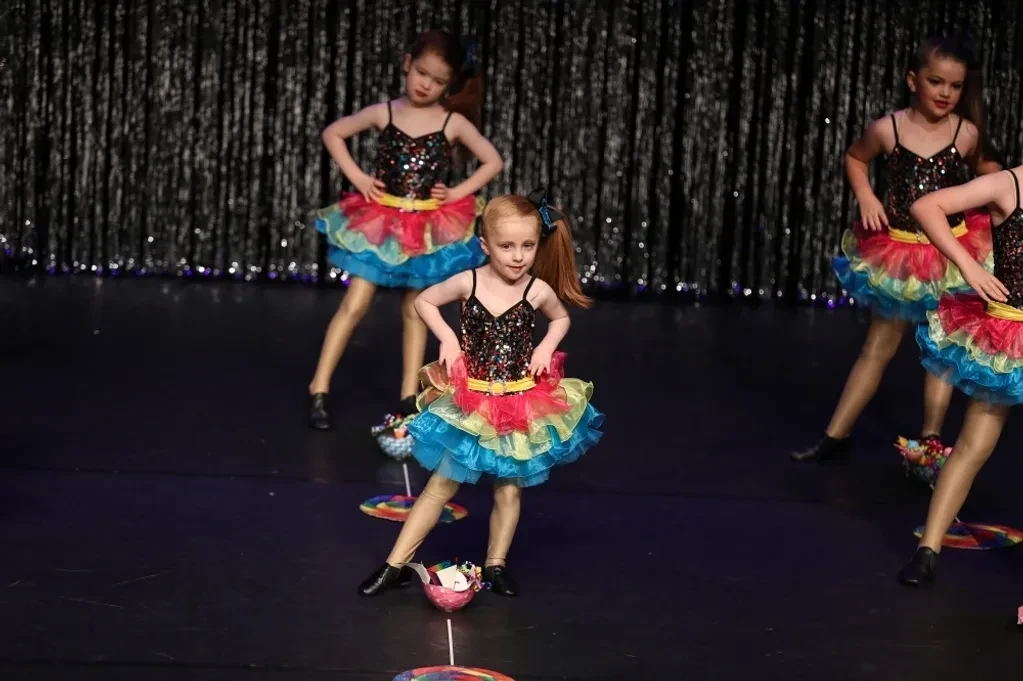 Young dancers in rainbow tutus with cupcake props performing on stage