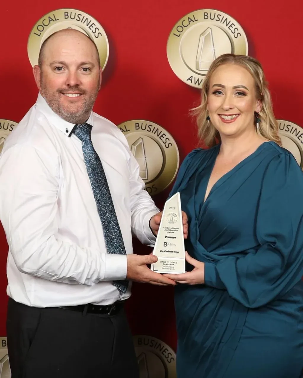 Two people smiling and holding Local Business Awards trophy at awards night