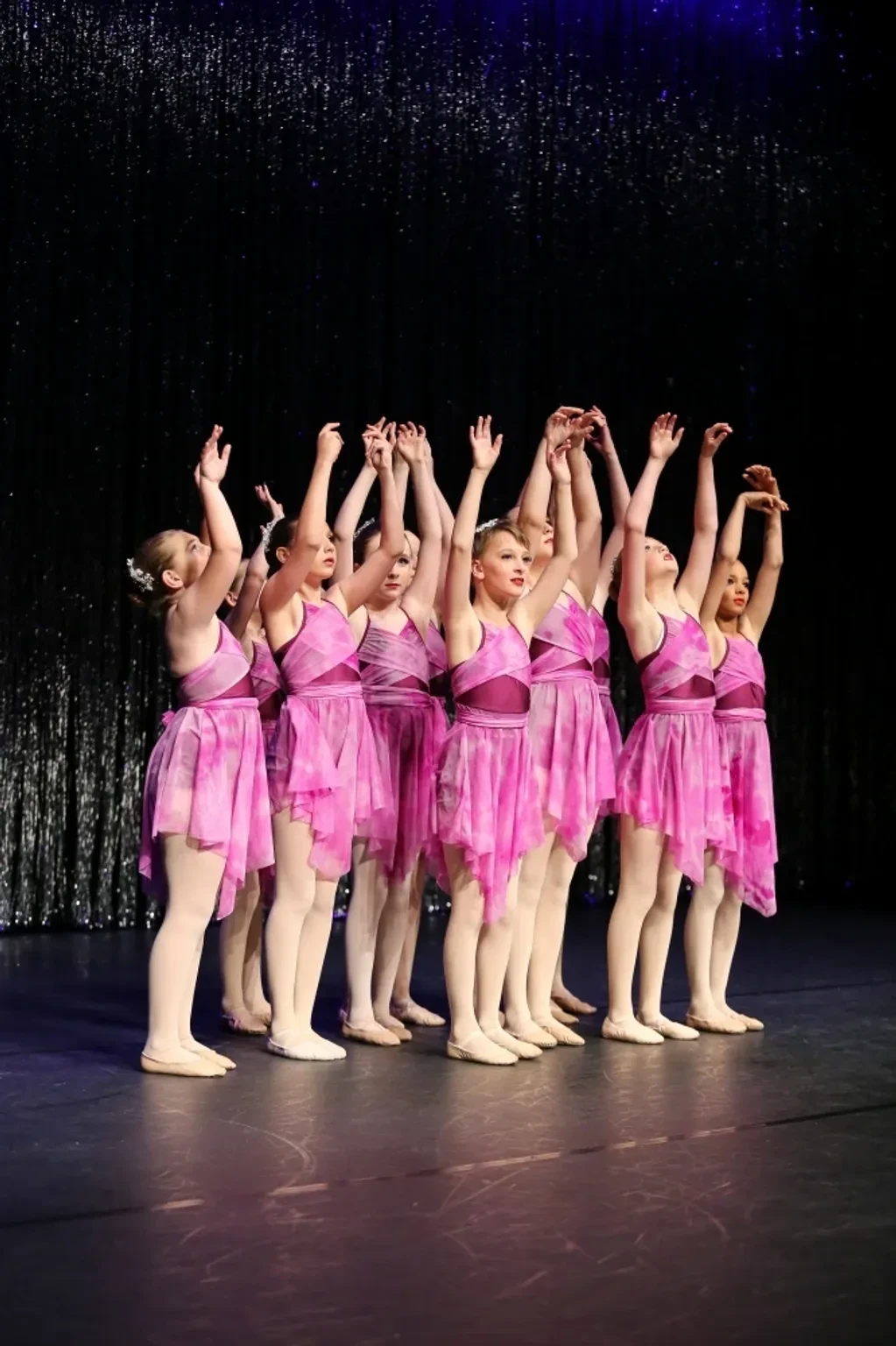 Young dancers in pink tutus performing on stage with arms raised